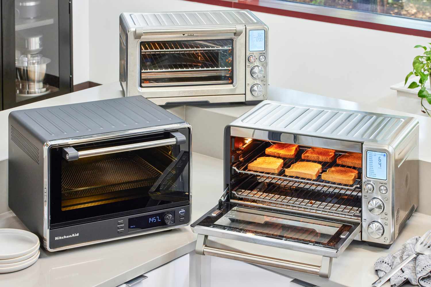 three toaster ovens on a countertop with one opened with toast inside