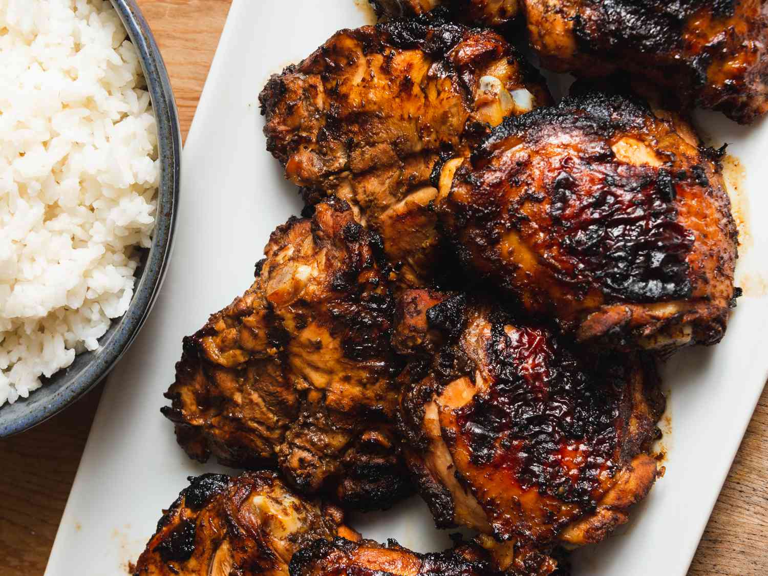 Closeup of grilled tamarind chicken thighs, served on a white platter.