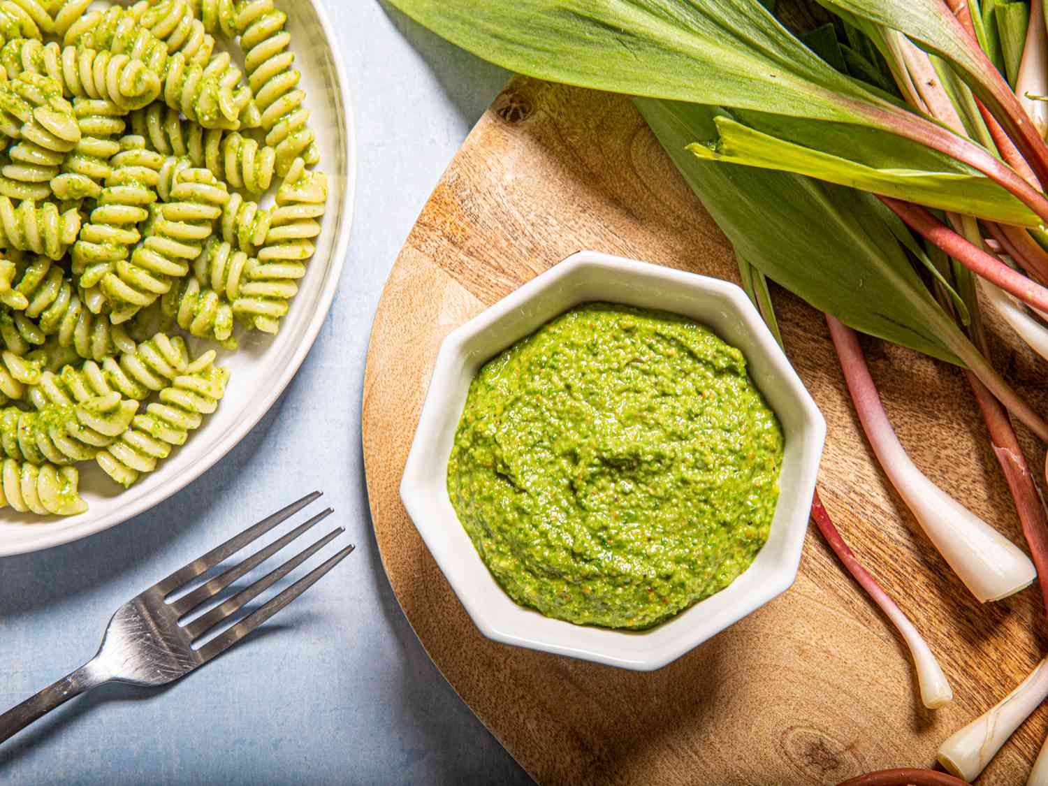 Overhead view of pesto in a small bowl next to ramps and pesto pasta