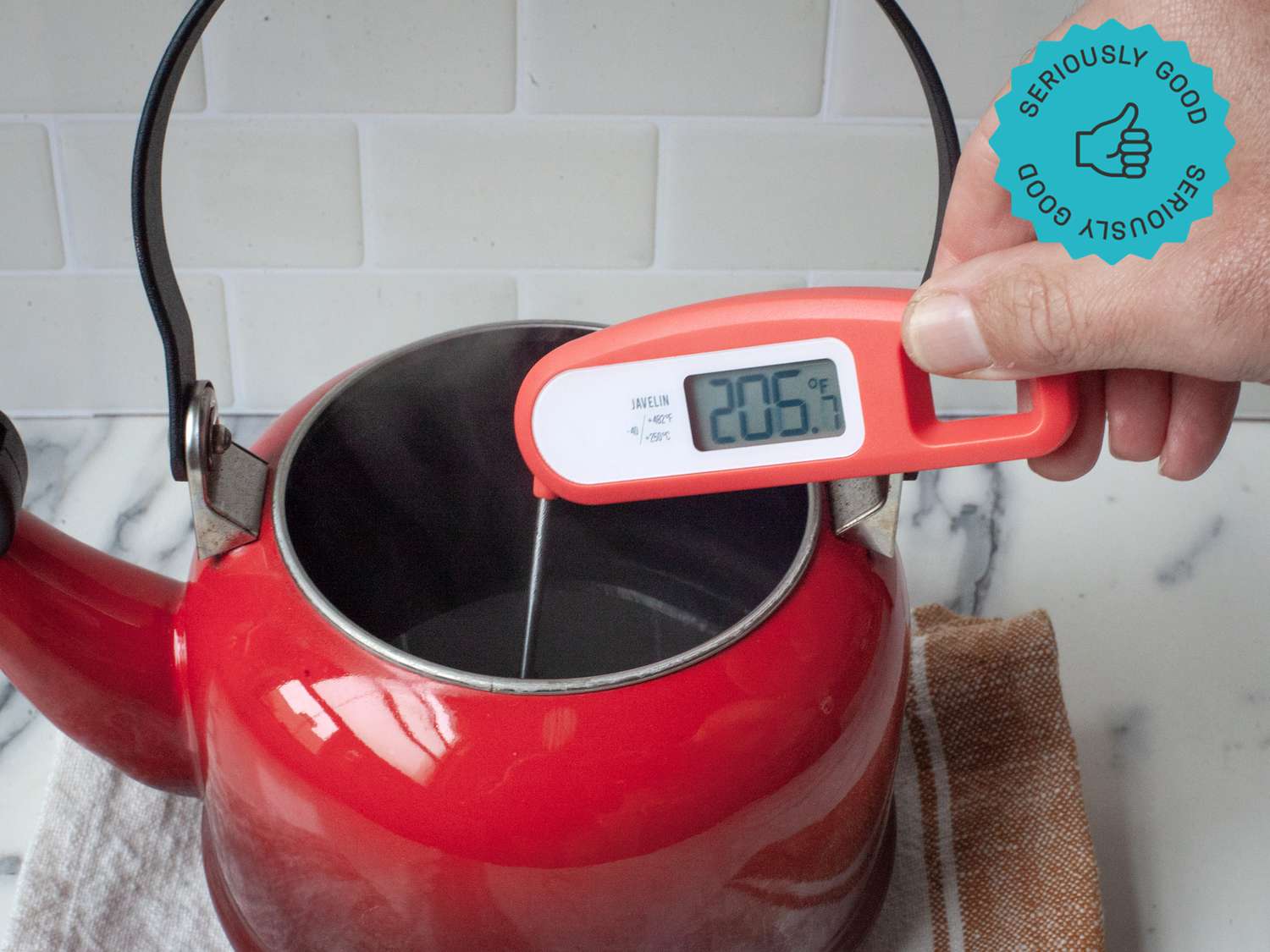 a person holding the lavatools javelin thermometer to measure the temperature of hot water in a tea kettle