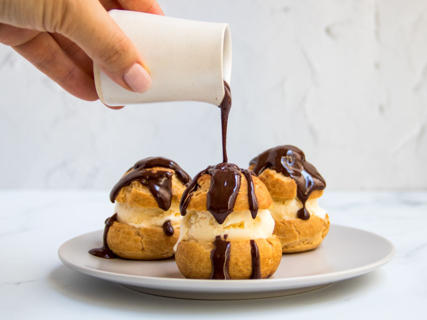 A trio of profiteroles being doused in chocolate sauce