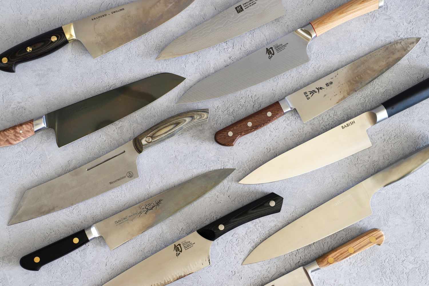 a variety of carbon steel chef's knives on a gray surface