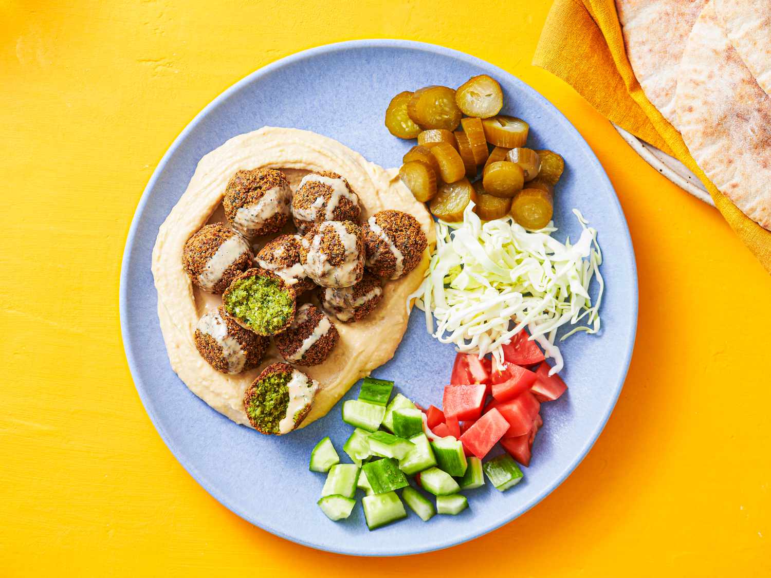 Plated pita bread stuffed with falafels, tahini, tomatoes, cucumber, pickles, and shredded cabbage.