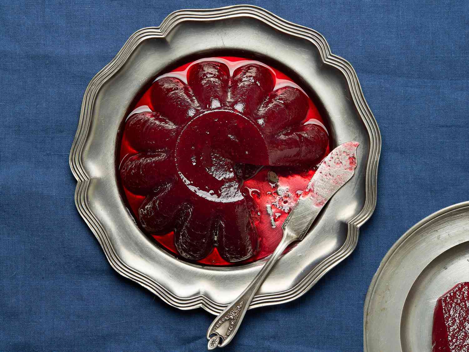 Silver platter of jellied cranberry sauce with a small plate of cranberry sauce in the bottom corner 