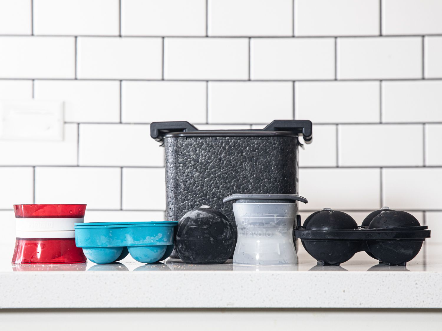 Several sphere ice molds against a white, subway tile background