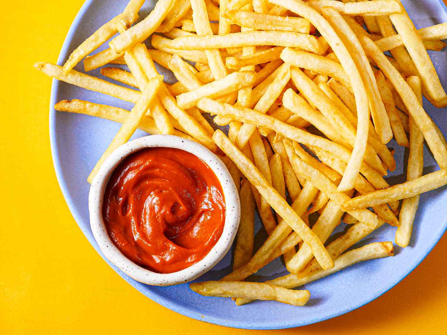 Overhead view of ketchup in a bowl on a plate with fries