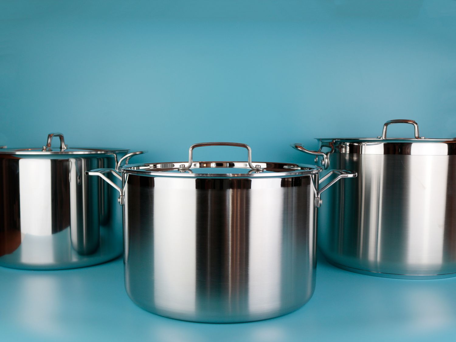 Three stainless steel stockpots on a blue surface