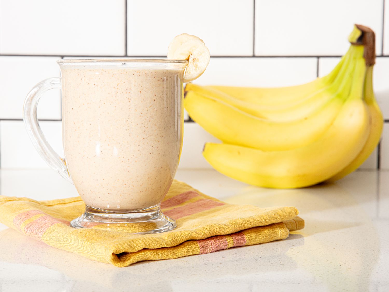 Banana smoothie in a glass cup with bananas in the background.