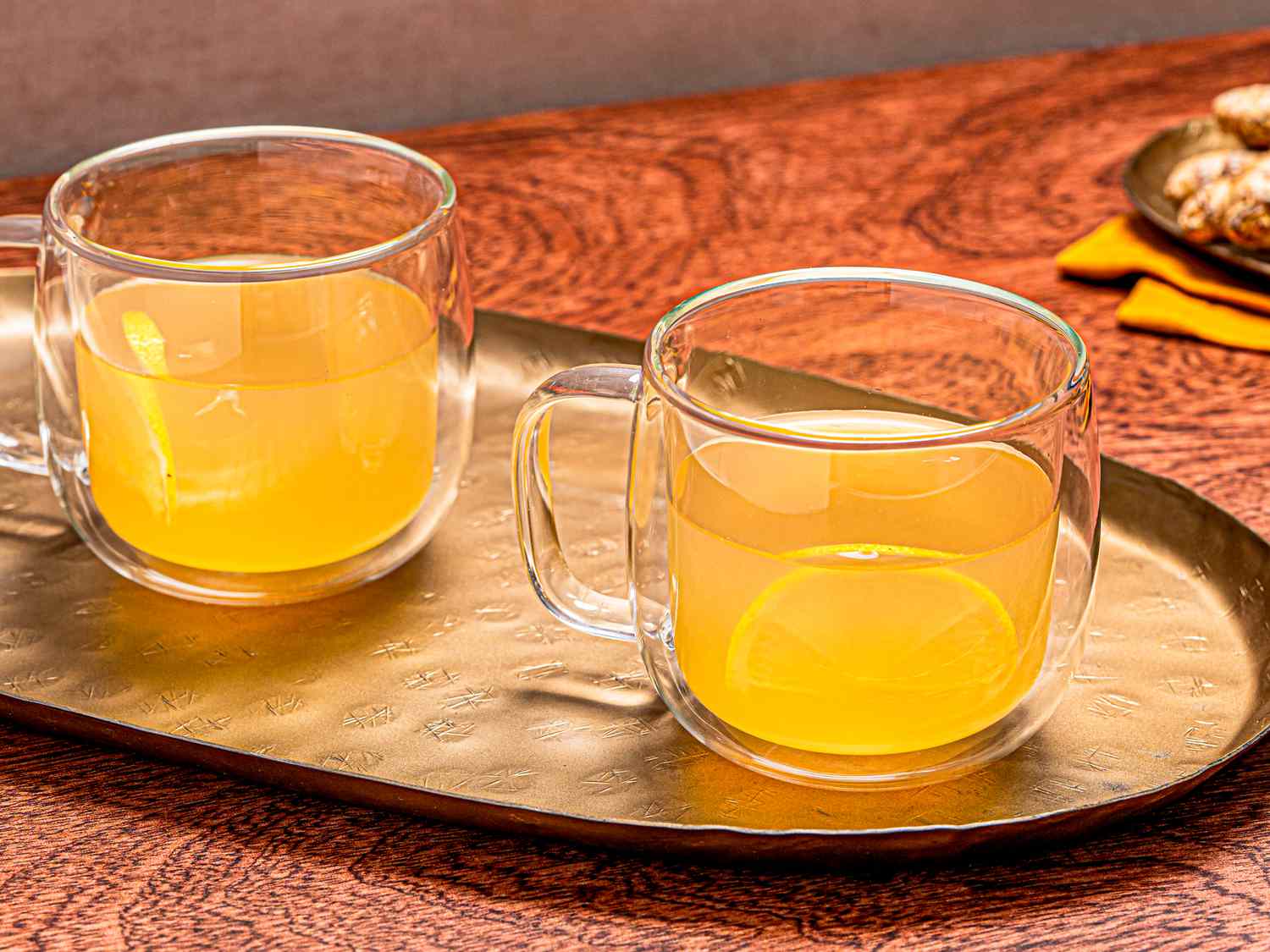 A metal tray with two ginger hot toddies served in glass mugs with lemon slices