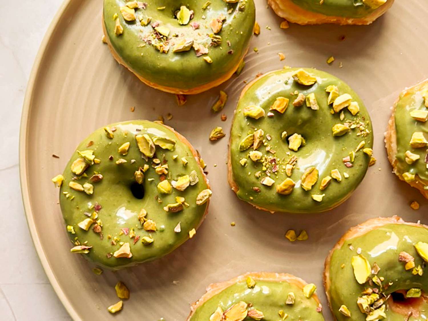 Doughnuts with pistachio cream and pistachios on top on a tan plate.