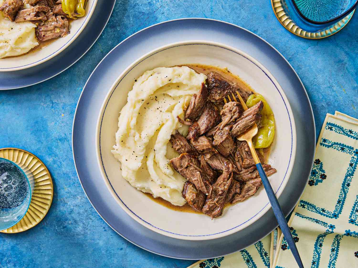 Mississippi Roast with mashed potatoes on blue plates and blue surface, Napkins and cups are blue and gold decor