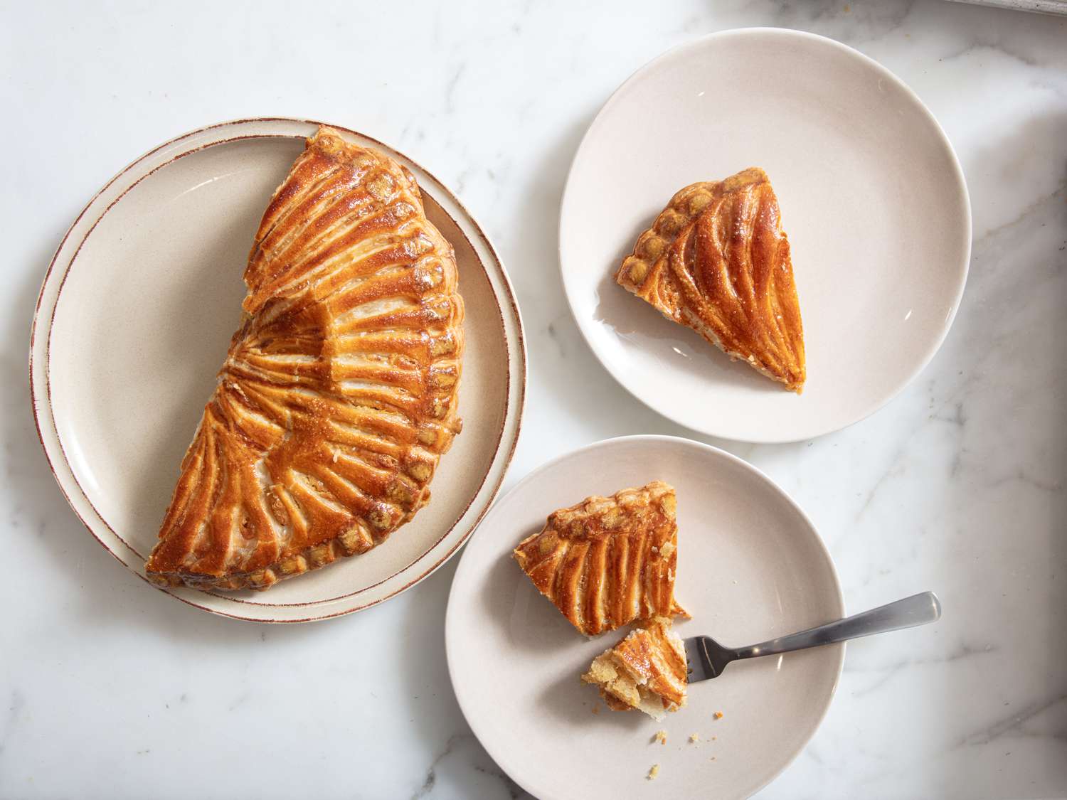 2 plates of Galette des Roi, one with a fork full of cake. A third plate with the remaining galette on it 