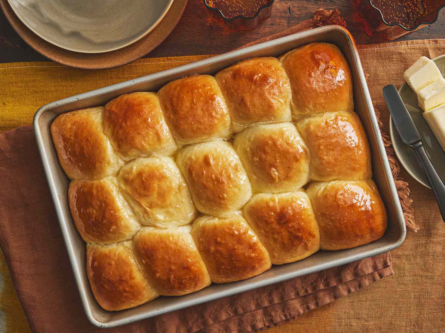 Tray of Parkerhouse Rolls, on a brown textile, with a side dish of butter and small serving dishes to the side. 